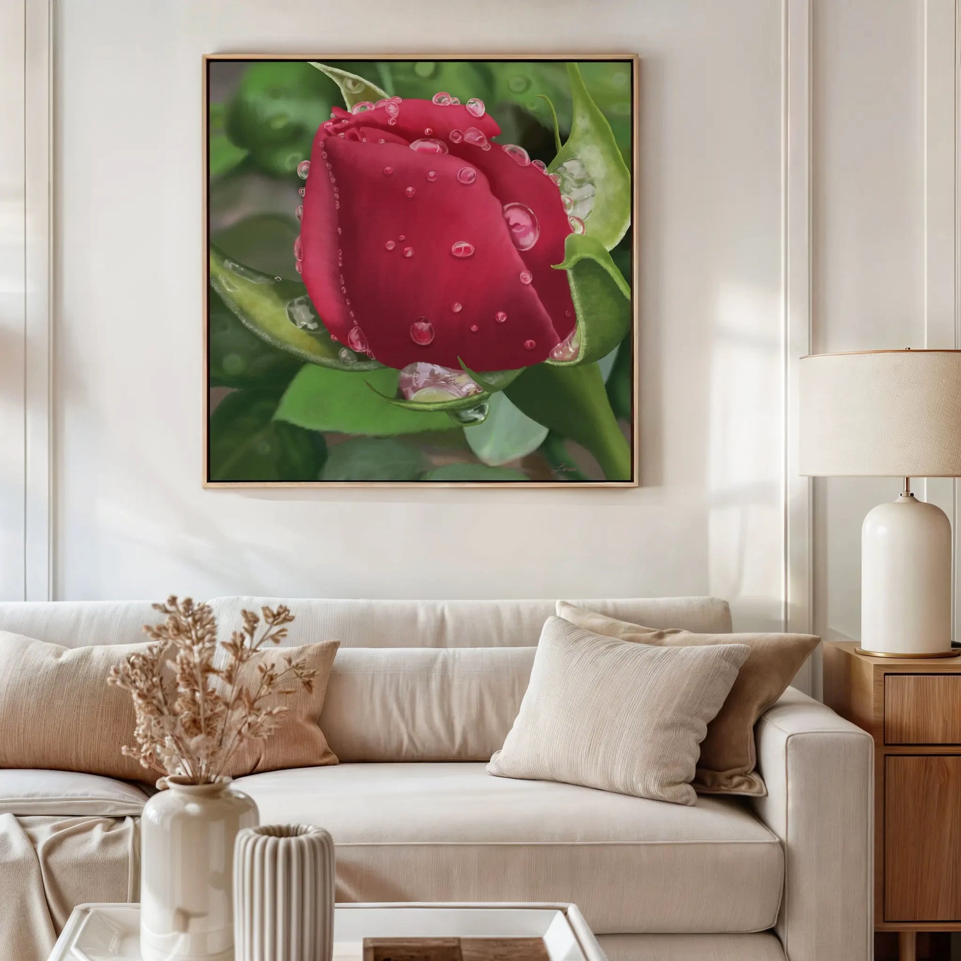 A modern living room features a white sofa, beige cushions, and a table with dried flowers. Above the sofa hangs a premium gallery-wrapped canvas of a red rosebud covered in water droplets, adding natural elegance wall art to the space.