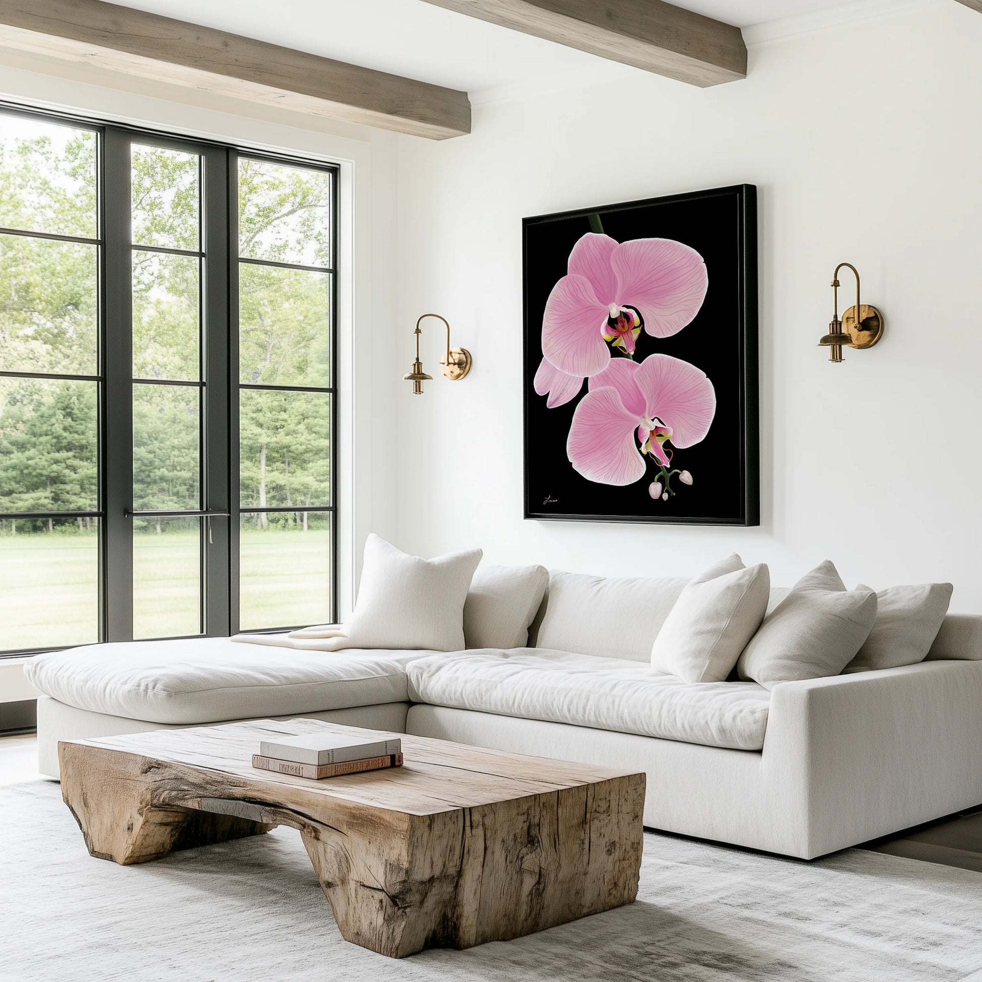 A modern living room features a white sectional sofa, light wood coffee table, neutral pillows, two brass wall sconces, and Midnight Bloom—an orchid flowers painting on premium canvas. Floor-to-ceiling windows reveal a green, wooded landscape outside.