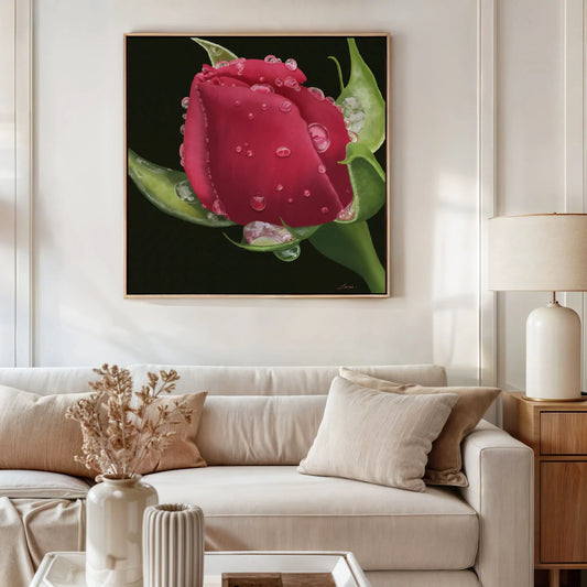 A modern living room with a beige couch, neutral cushions, a side table with a light lamp, and a vase of dried flowers. Above the sofa hangs a gallery-wrapped canvas featuring a hyperrealistic red rose titled Deeper Love.
