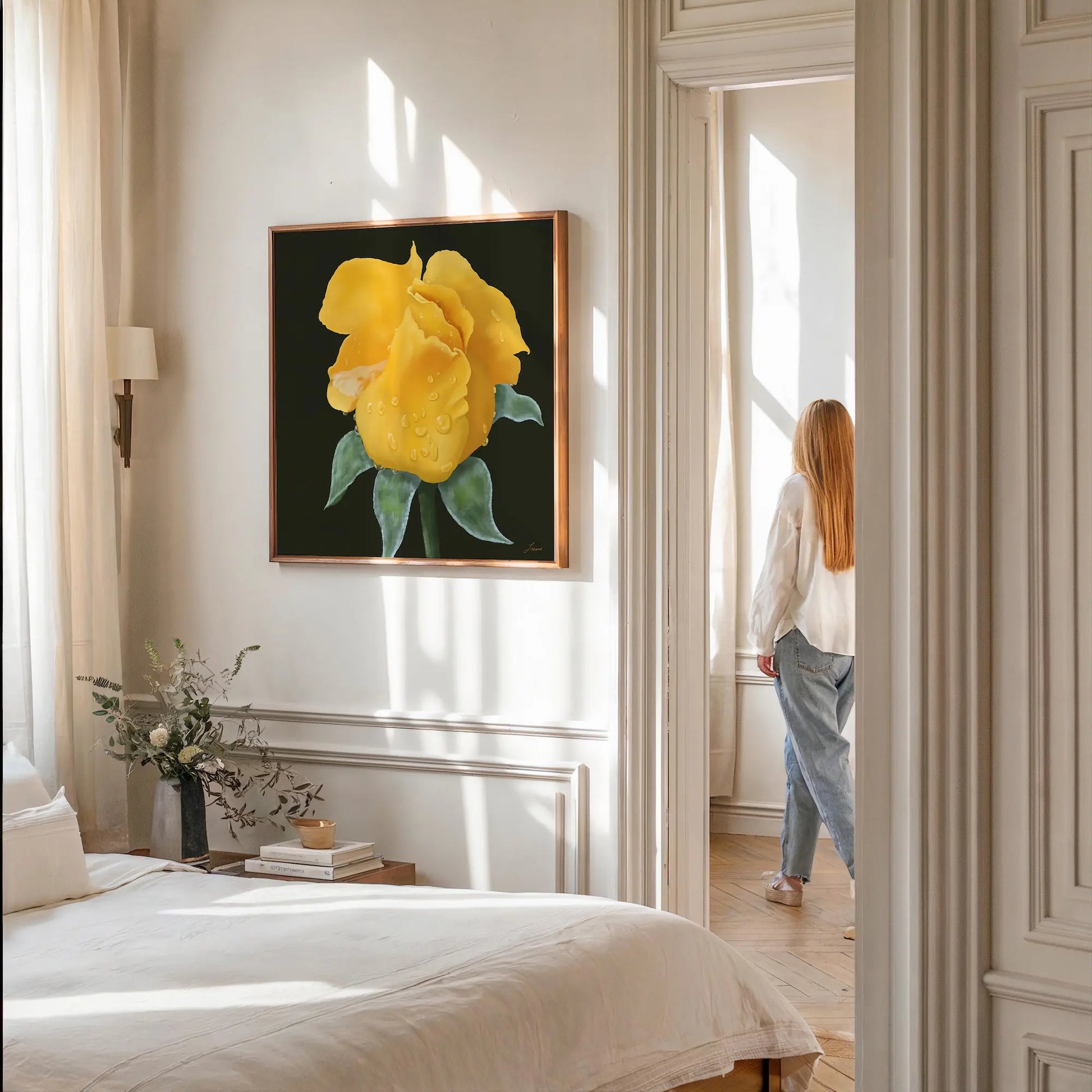 A sunlit bedroom with white walls and bedding features yellow rose artwork on a gallery-wrapped canvas. A person with long, light hair, wearing a white top and jeans, stands near a bright window. A vase of flowers sits on the bedside table.