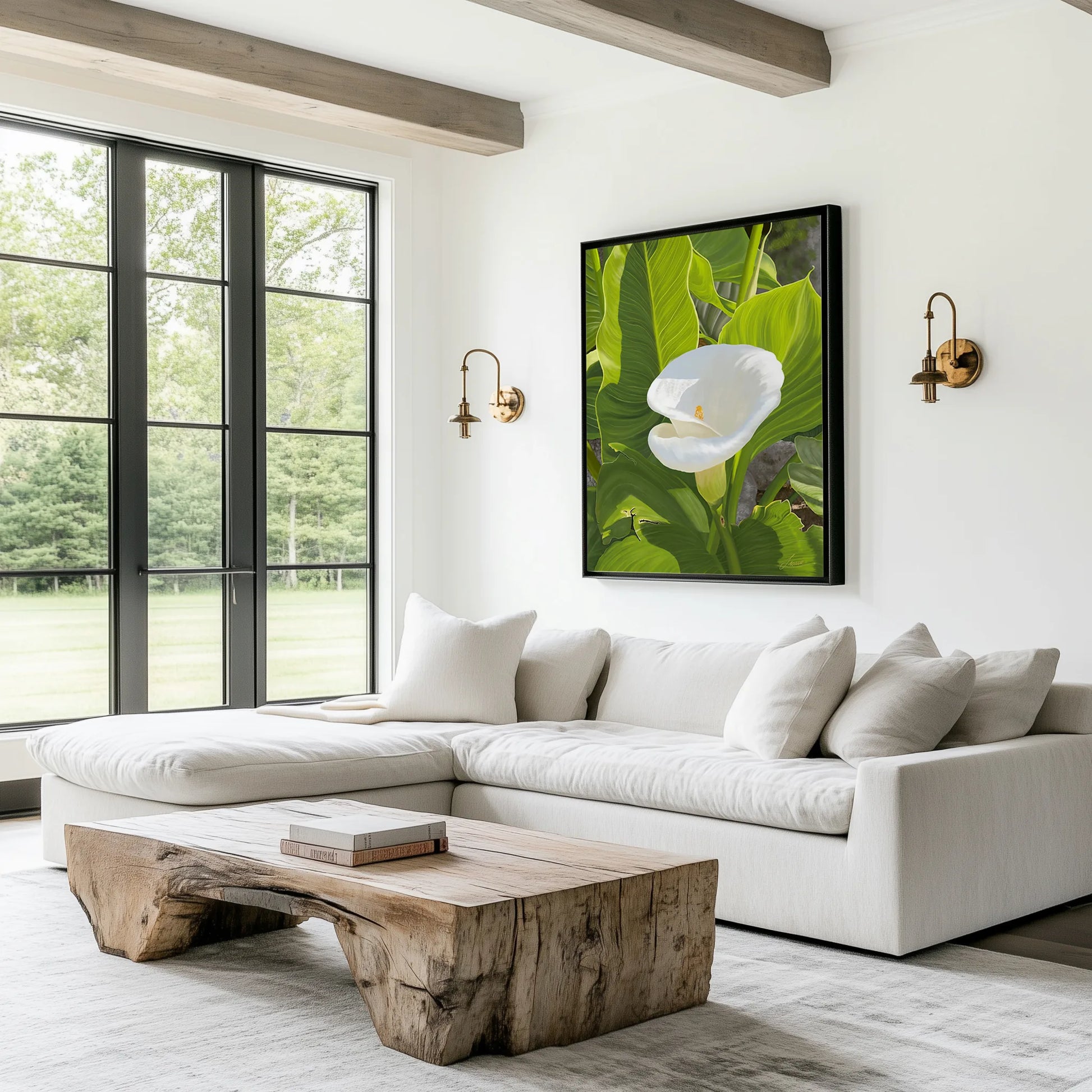 A bright, modern living room with a white sectional sofa, rustic wooden coffee table, large windows, and a wall adorned with a gallery-wrapped canvas featuring hyper-realistic detail of calla lilies and green leaves. Brass wall sconces flank the painting.