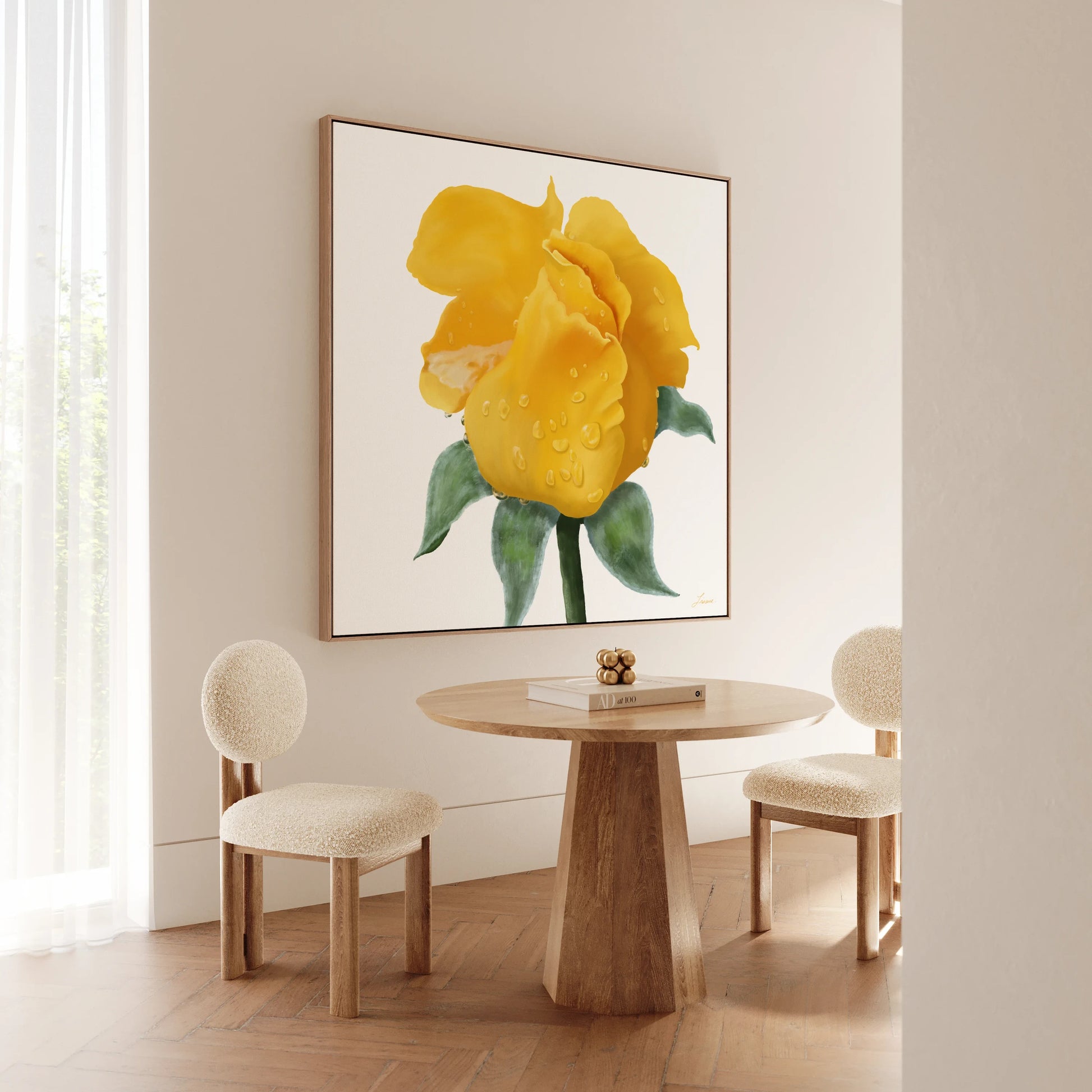 A small round wooden table with two cream-colored, cushioned chairs sits in a bright room with wooden floors. On the wall hangs a gallery-wrapped canvas featuring a yellow rose with water droplets and green leaves. Light streams in from sheer curtains on the left.