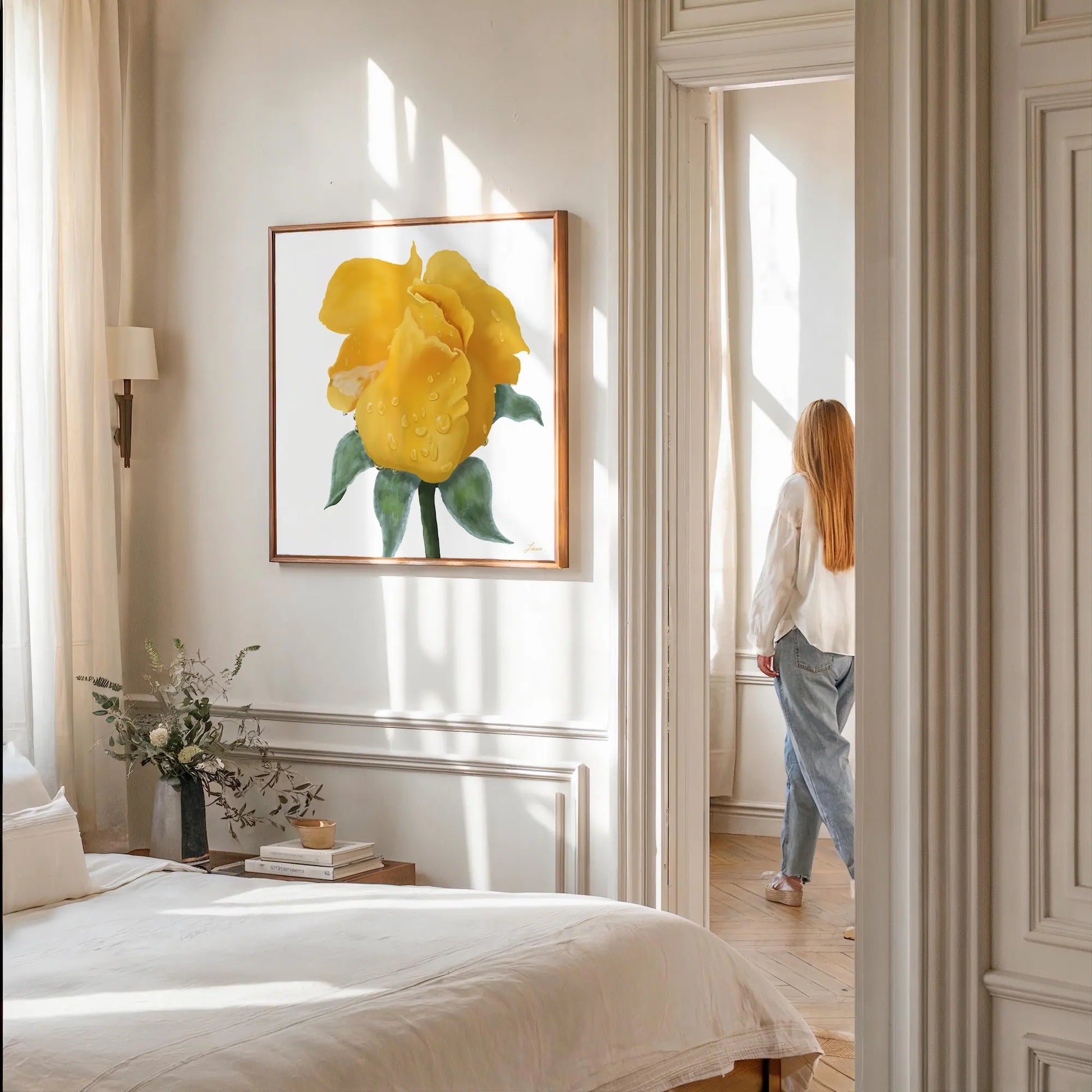 A sunlit bedroom with beige walls features a bed with white bedding, a nightstand holding a vase of flowers, and a vibrant color gallery-wrapped canvas of a yellow rose. A woman with long hair stands by the bright window in the adjoining room.