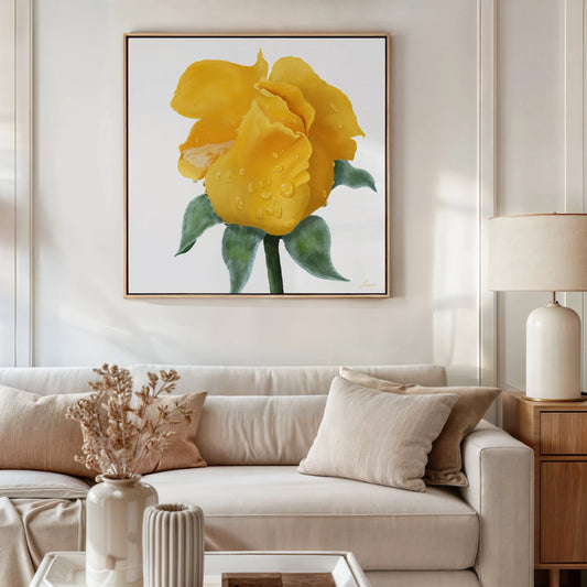 A modern living room with neutral tones features a beige sofa, cream pillows, dried flowers in a white vase, a table lamp, and a yellow rose gallery-wrapped canvas with water droplets and green leaves above the sofa.
