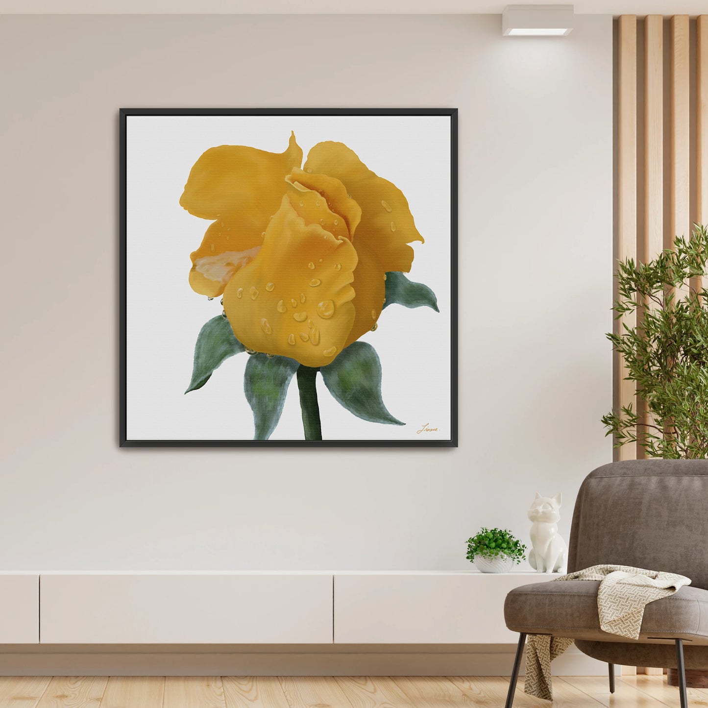 A modern living room with a large canvas art print of a vibrant yellow rose with water droplets on a white background, hung on a beige wall above a low white cabinet. A plant, small cat figurine, and cozy blanket complete the minimalist decor.